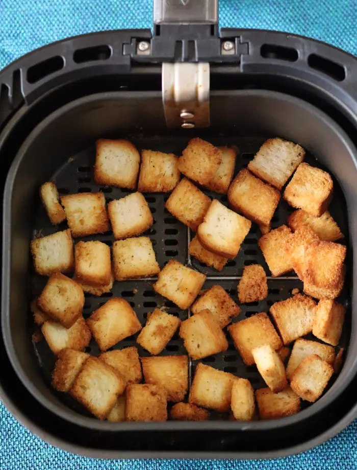 Seasoned bread cubes spread in a single layer in the air fryer basket