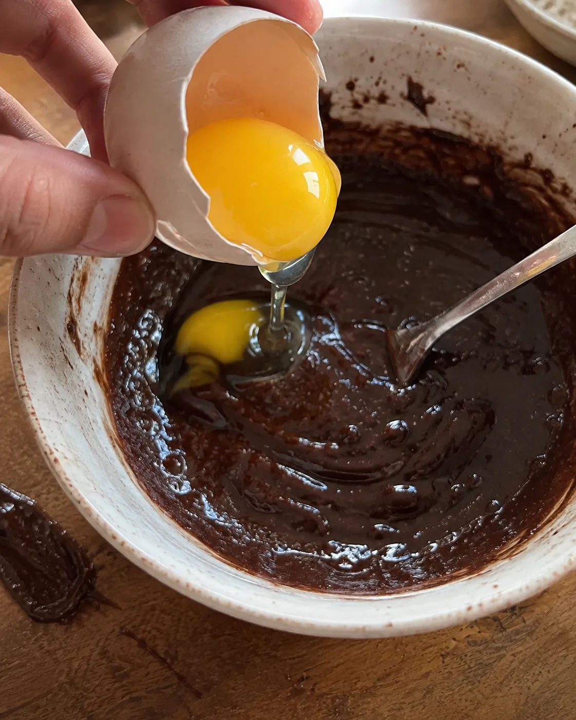 An egg yolk being tipped from the shell into chocolate batter in a ramekin