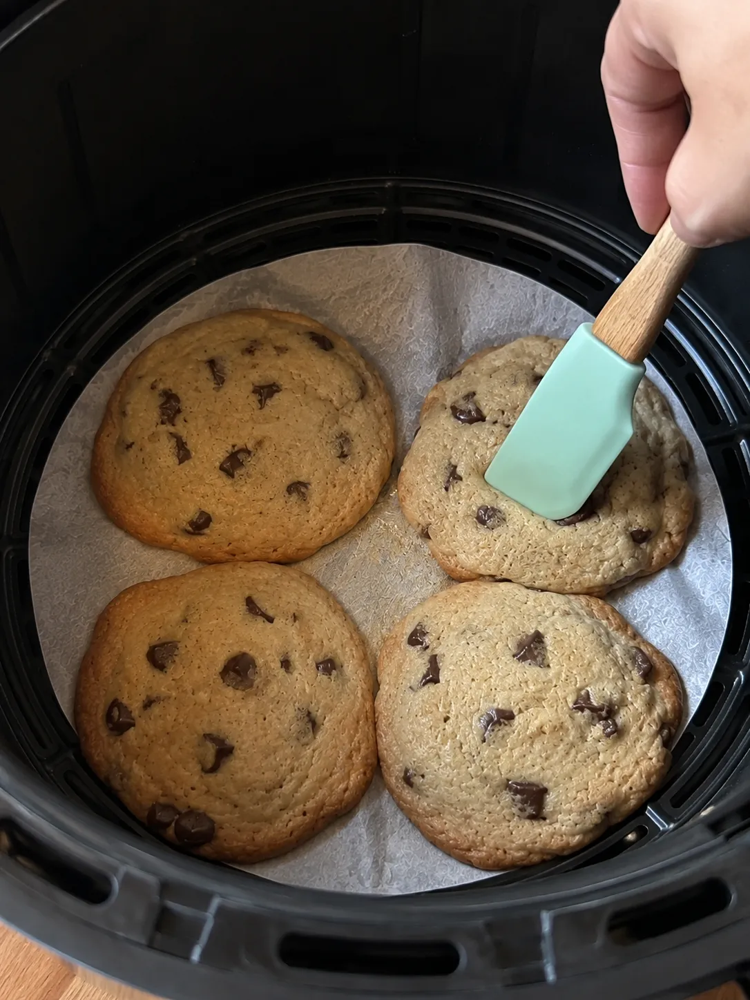 A spatula lifting one of four golden baked cookies from an air fryer basket