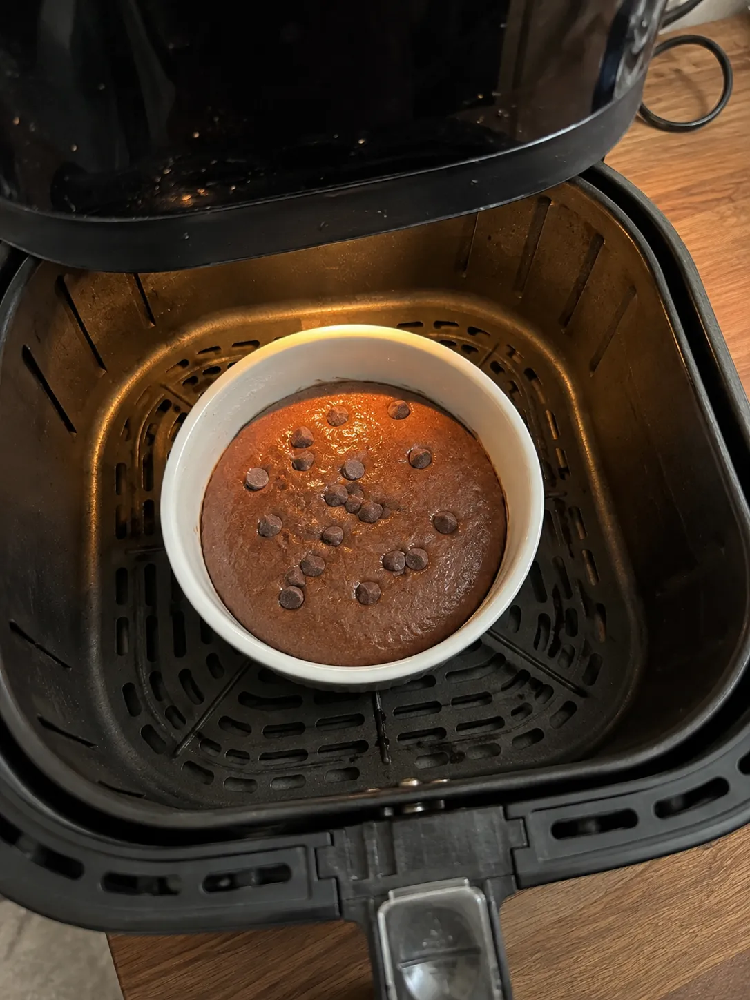 A baked chocolate mug cake in a white ramekin sitting in an air fryer basket