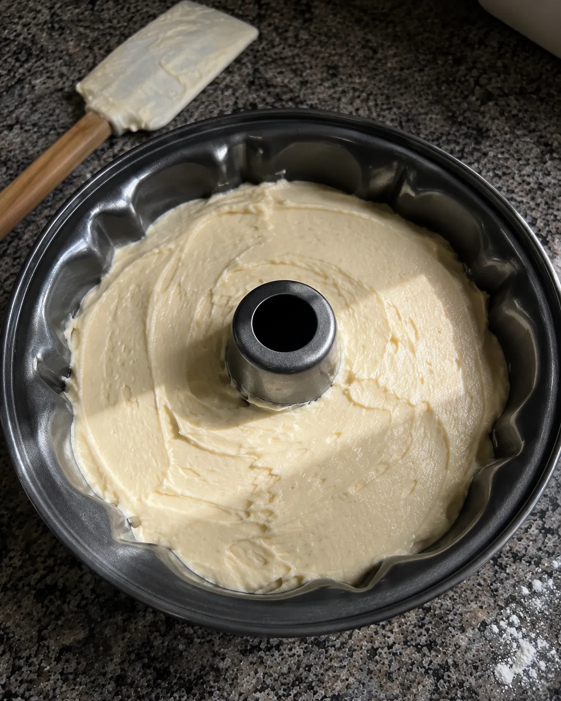 Pound cake batter smoothed into a fluted tube pan, with the metal center column standing clear of the batter