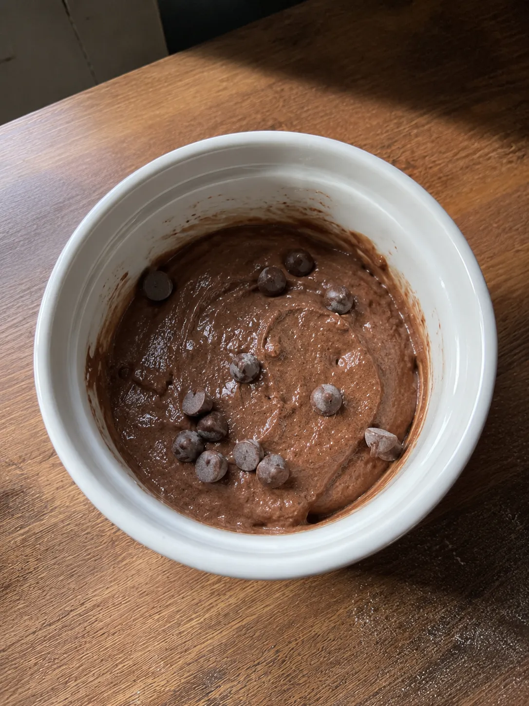 Chocolate mug cake batter mixed and levelled in a white ramekin, filled less than halfway, with chocolate chips scattered over the top