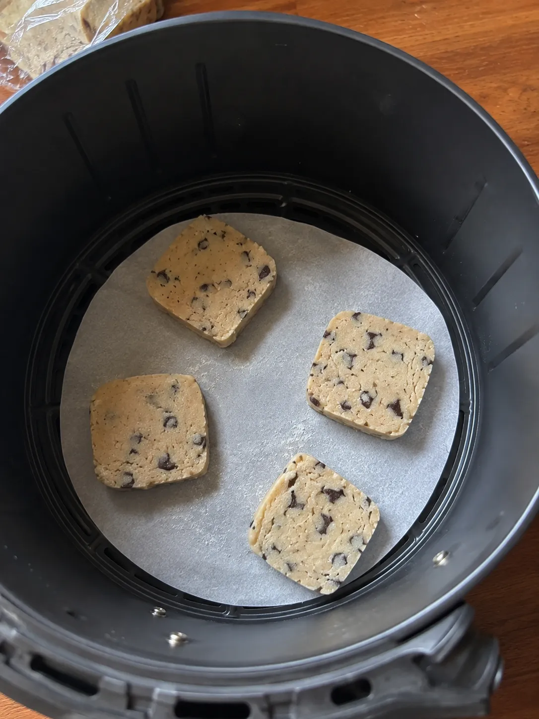 Four squares of refrigerated cookie dough spaced apart on parchment in an air fryer basket