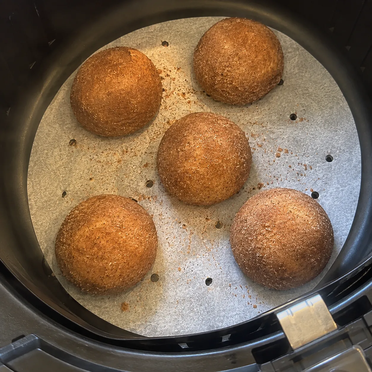 Five cinnamon sugar dough balls puffed into smooth domes in an air fryer basket
