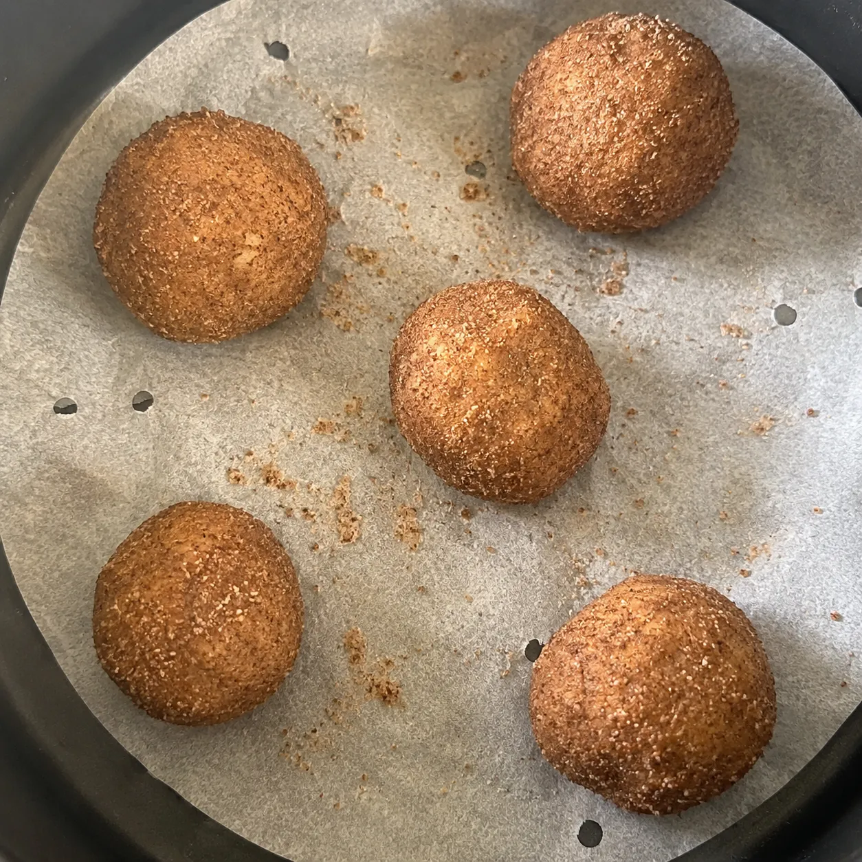 Five coated snickerdoodle dough balls spaced apart on perforated parchment in an air fryer basket