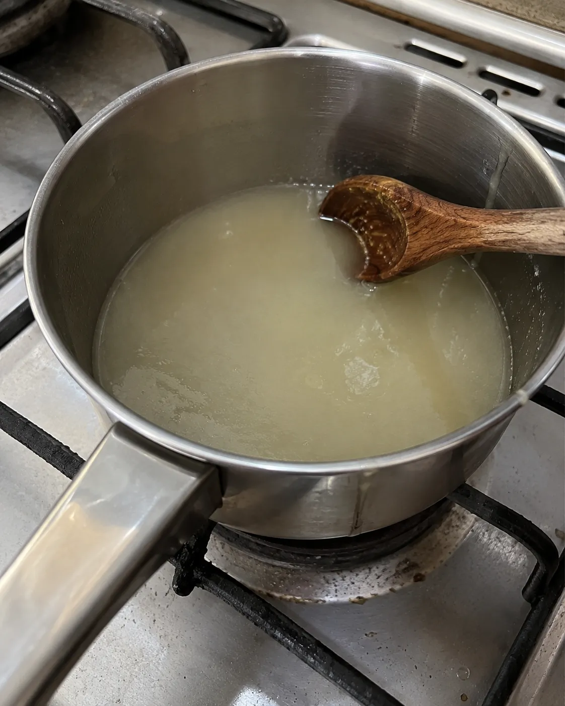 Lemon juice and sugar being warmed in a small saucepan on the stovetop, still cloudy and not yet fully dissolved