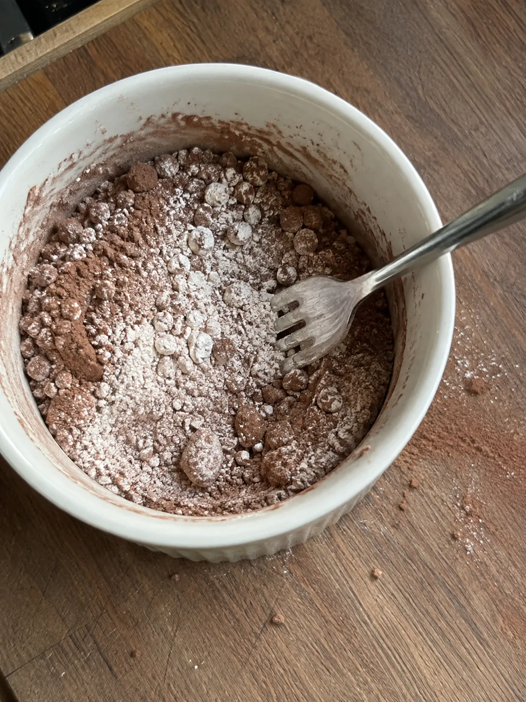 Flour, sugar, cocoa powder, baking powder and salt being whisked together with a fork in a white ramekin