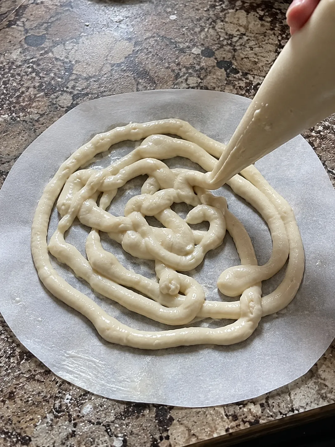 Funnel cake batter being piped in overlapping loops onto a buttered parchment round