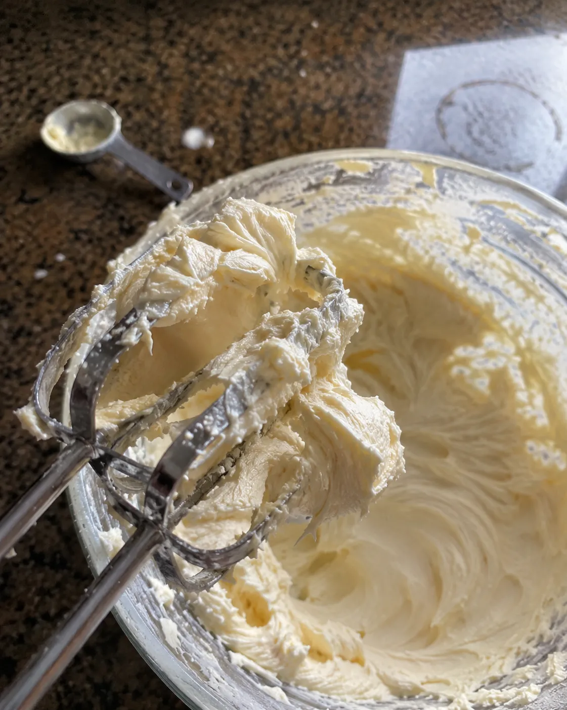 Smooth beaten cream cheese clinging to electric beaters over a glass bowl with no lumps visible