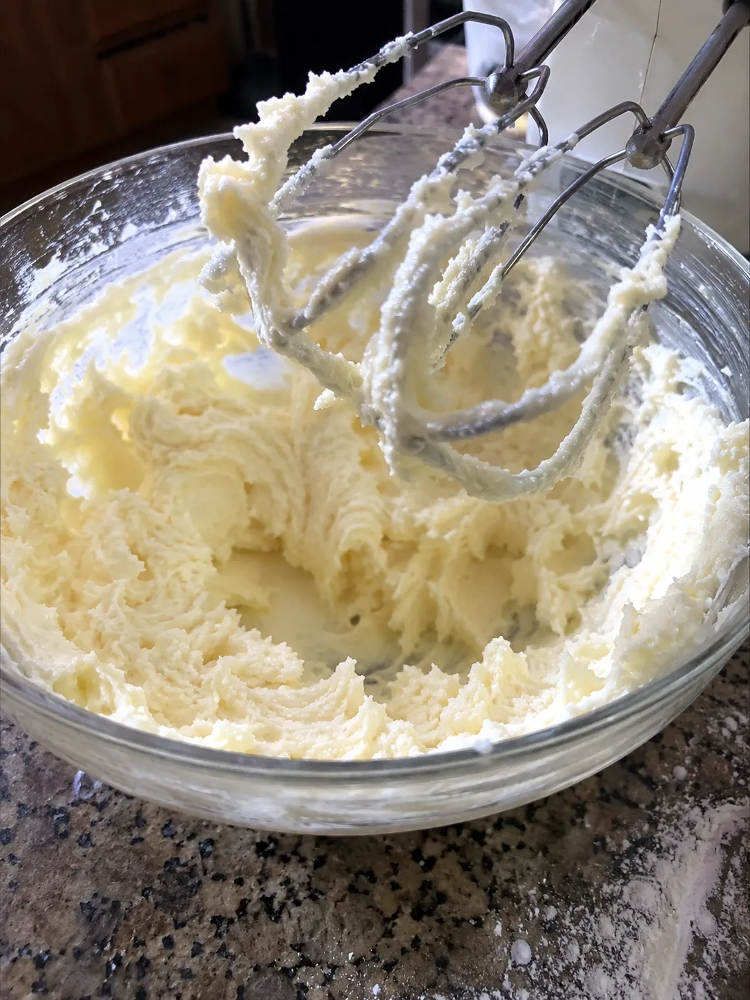 Pale, aerated creamed butter and sugar clinging to hand mixer beaters lifted out of a glass bowl