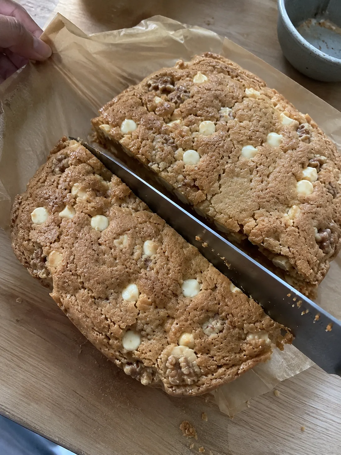 A long knife cutting a cooled blondie slab that has been lifted out on its parchment sling