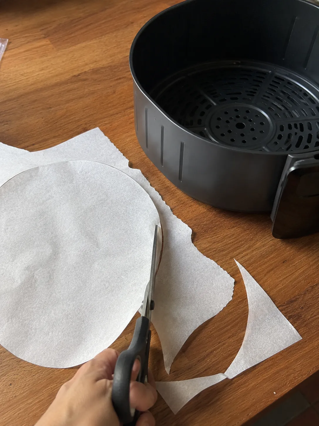 Cutting a circle of parchment to fit a round air fryer basket, with the basket alongside
