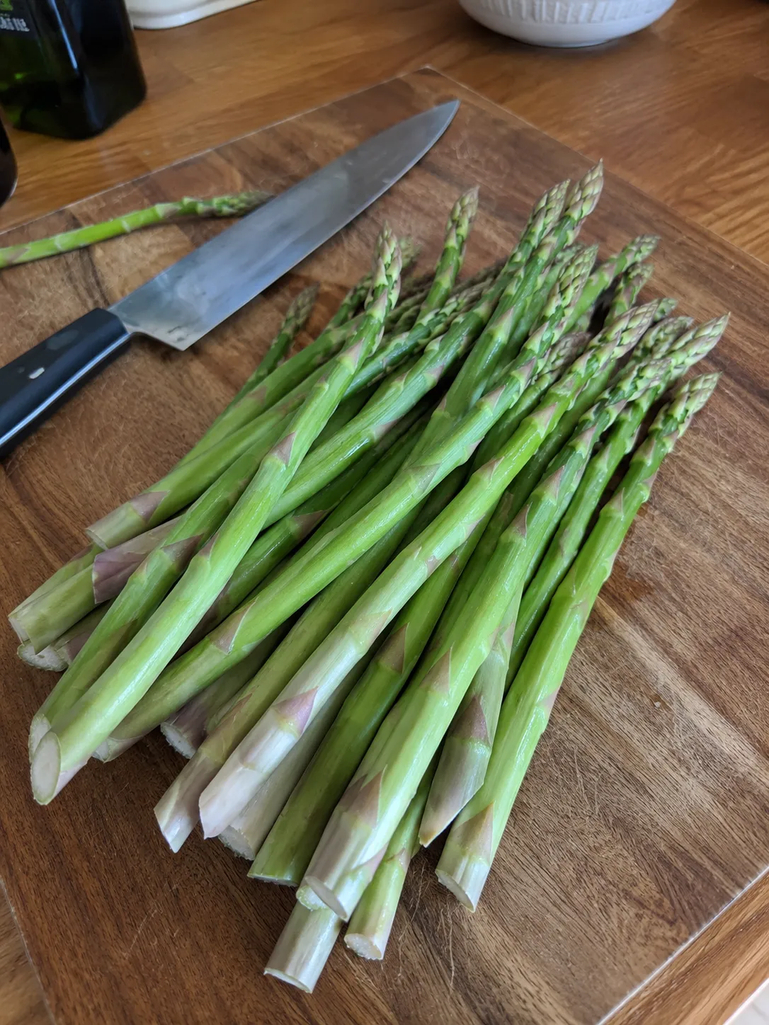 A bundle of raw asparagus spears on a wooden cutting board with a chef's knife
