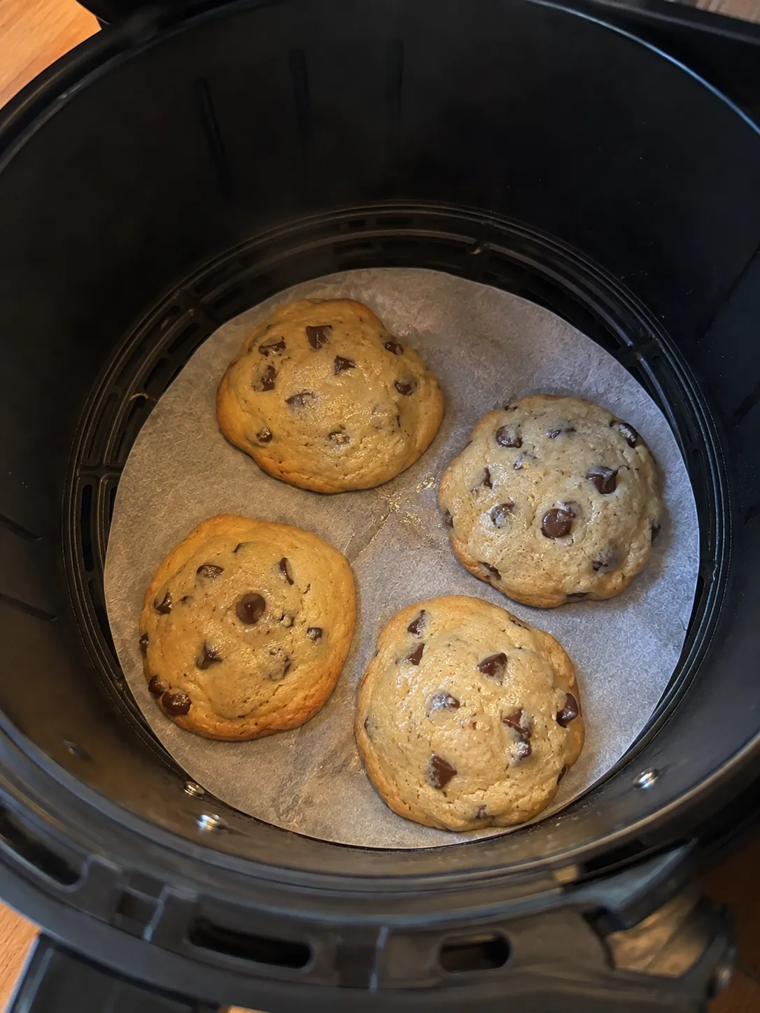Four pale cookies in an air fryer basket with edges just set and centers still glossy