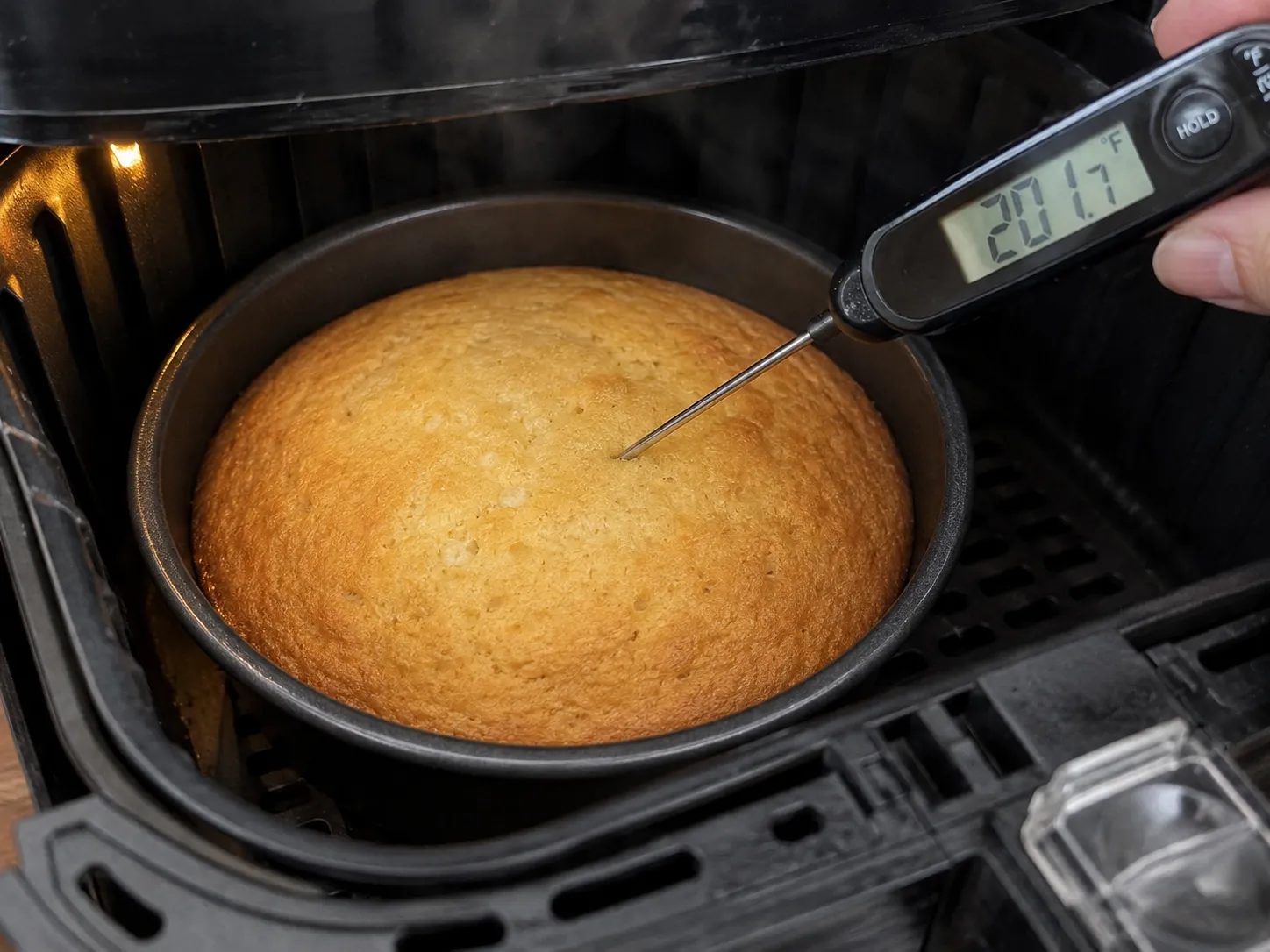 An instant-read thermometer reading 201.7 degrees Fahrenheit pushed into a cake in an air fryer basket