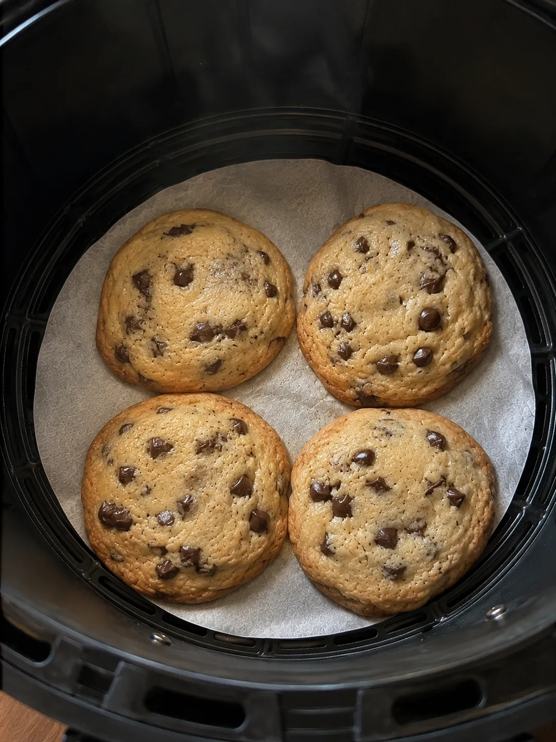 Four baked cookies spread almost to touching on parchment in a round air fryer basket