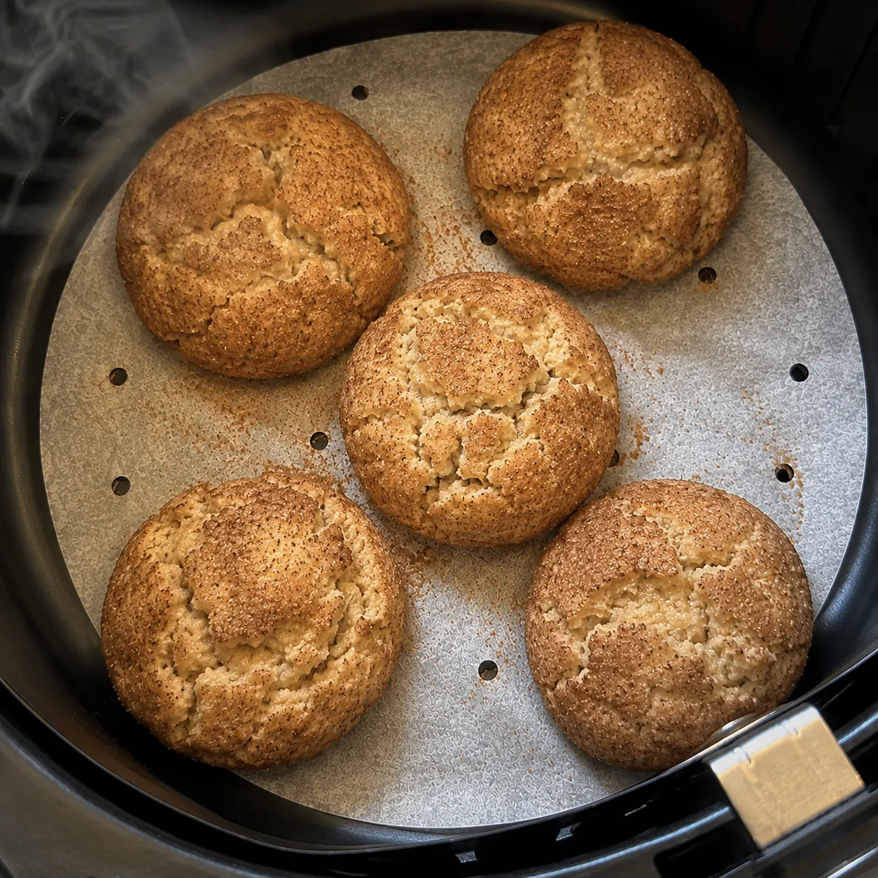 Five baked snickerdoodles fallen and cracked on parchment in an air fryer basket