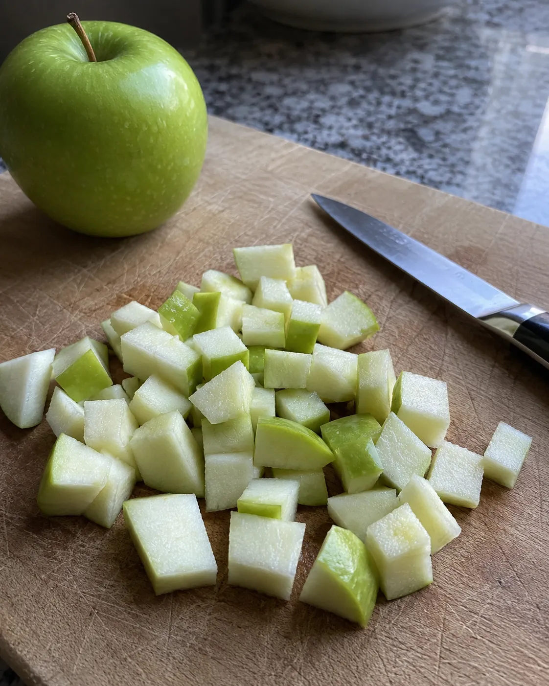 A whole Granny Smith apple beside evenly diced half inch cubes on a wooden board