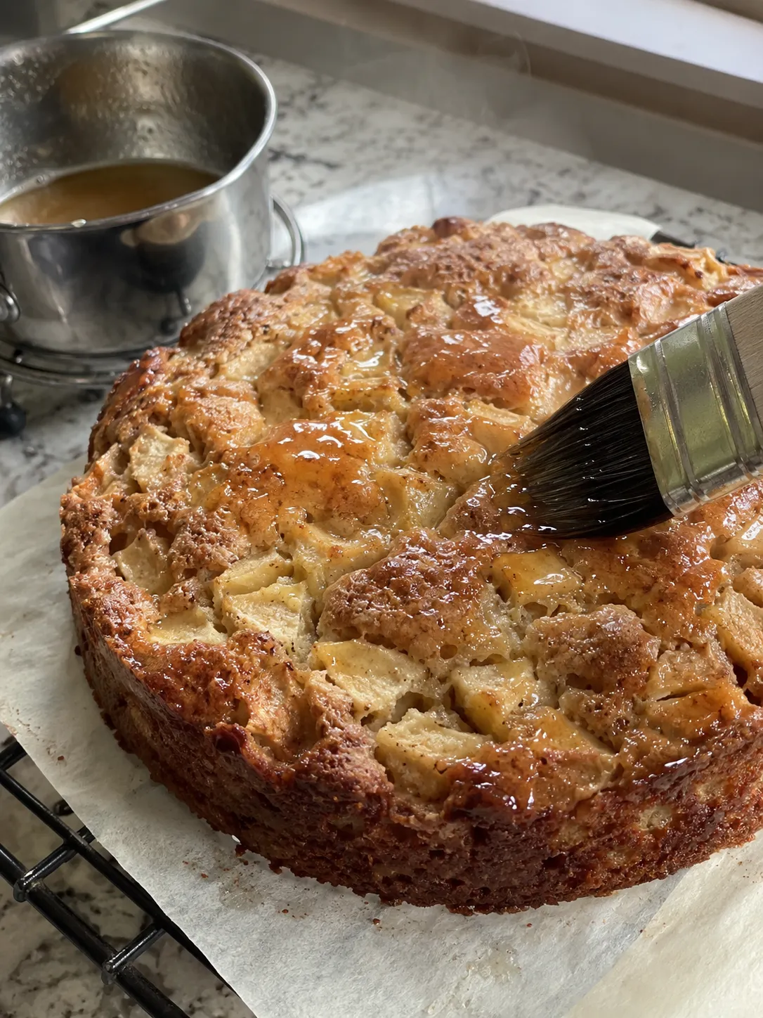 A pastry brush spreading amber apple syrup over the top of a freshly baked apple cake