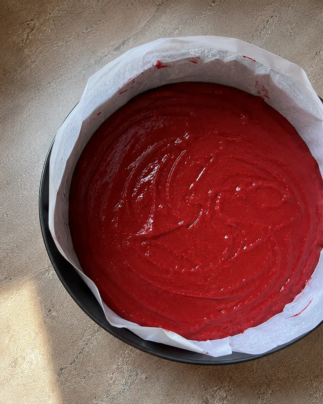 Red velvet cake batter smoothed into a parchment-lined pan, ready to go into the air fryer