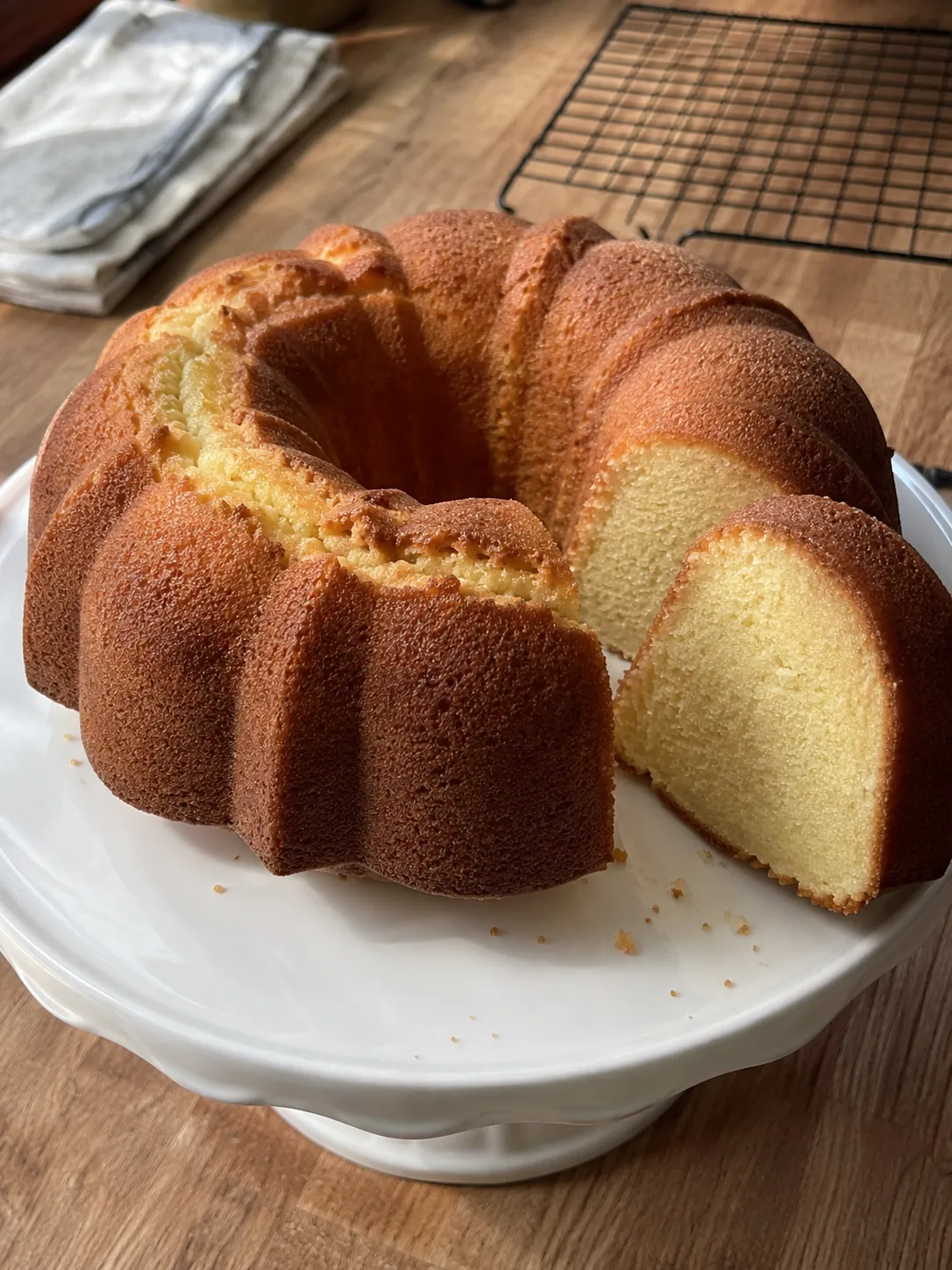 A golden ring-shaped air fryer pound cake on a white plate with one wedge pulled forward, showing a tight even buttery crumb