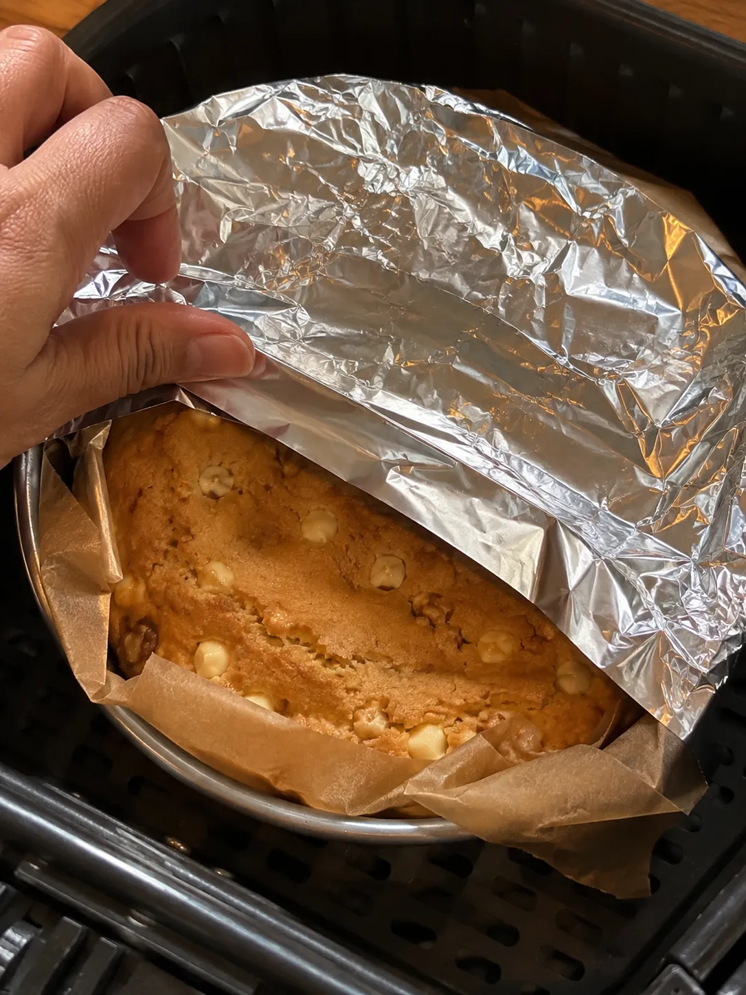 A sheet of foil being laid over a golden blondie baking in an air fryer basket