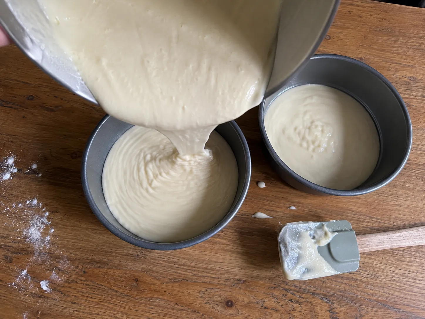 Cake batter being poured from a mixing bowl into two round metal cake pans