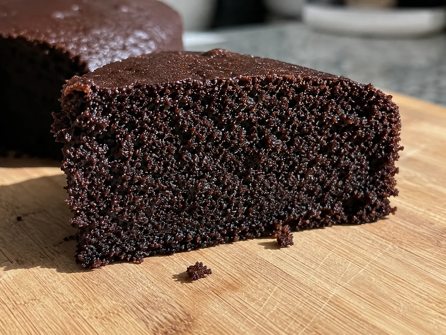 Close-up of a cut wedge of dark chocolate cake on a wooden board, the crumb open and glistening all the way out to the crust