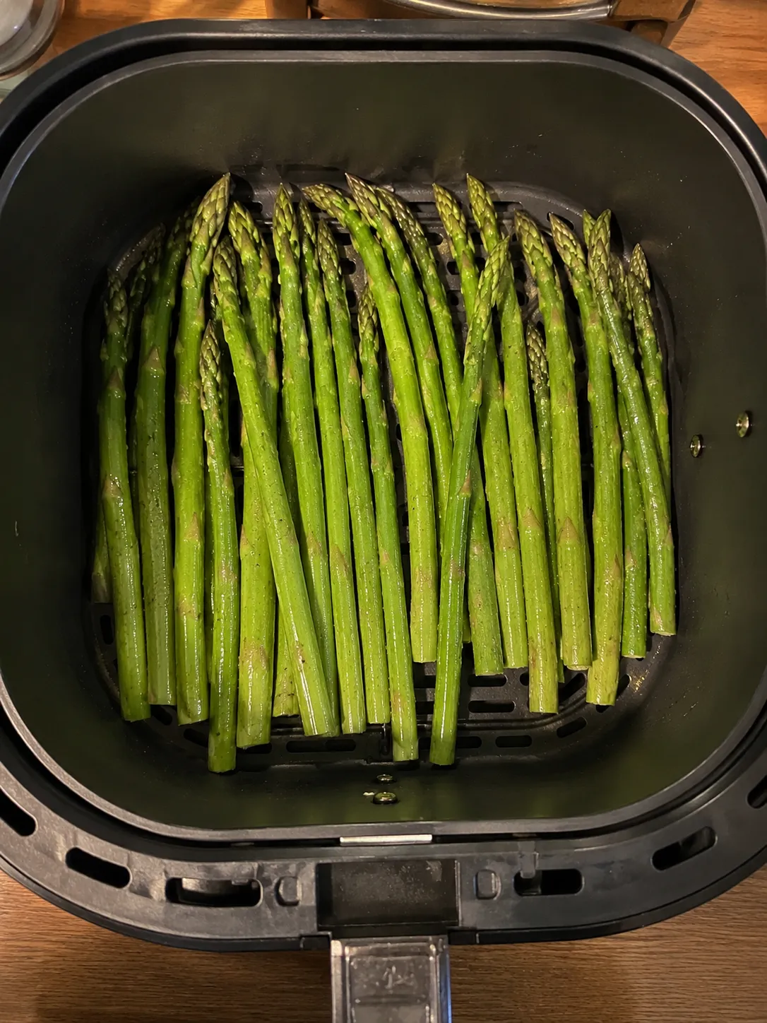 Raw oiled asparagus spears laid in a single layer in an air fryer basket