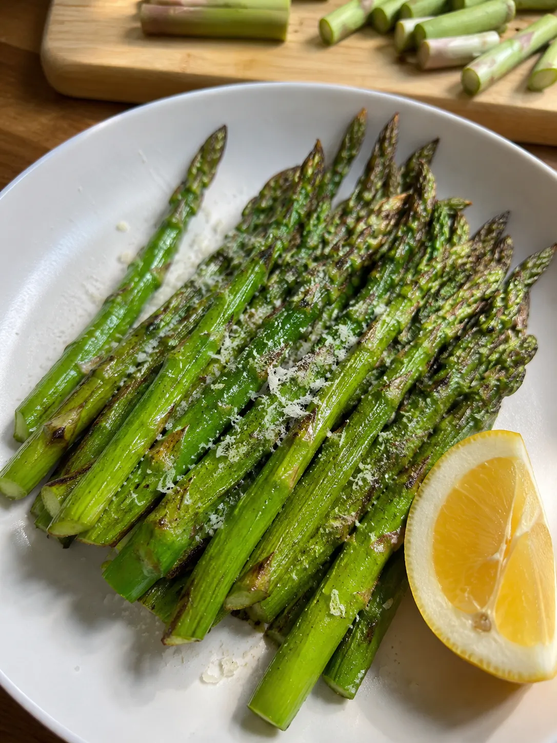 Air fryer asparagus on a white plate with grated parmesan and a lemon wedge