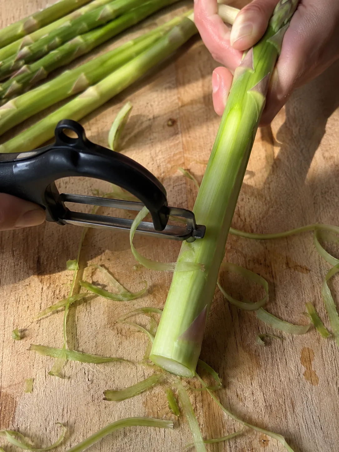 A vegetable peeler taking the outer layer off the bottom of a thick asparagus spear