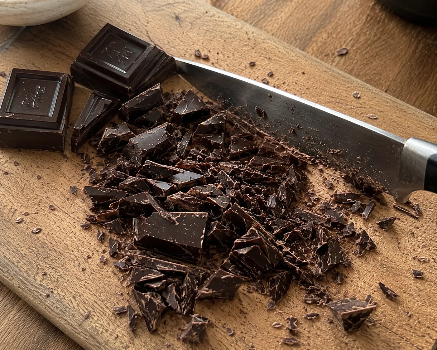 Dark chocolate being chopped into irregular pieces on a wooden board with a chef's knife