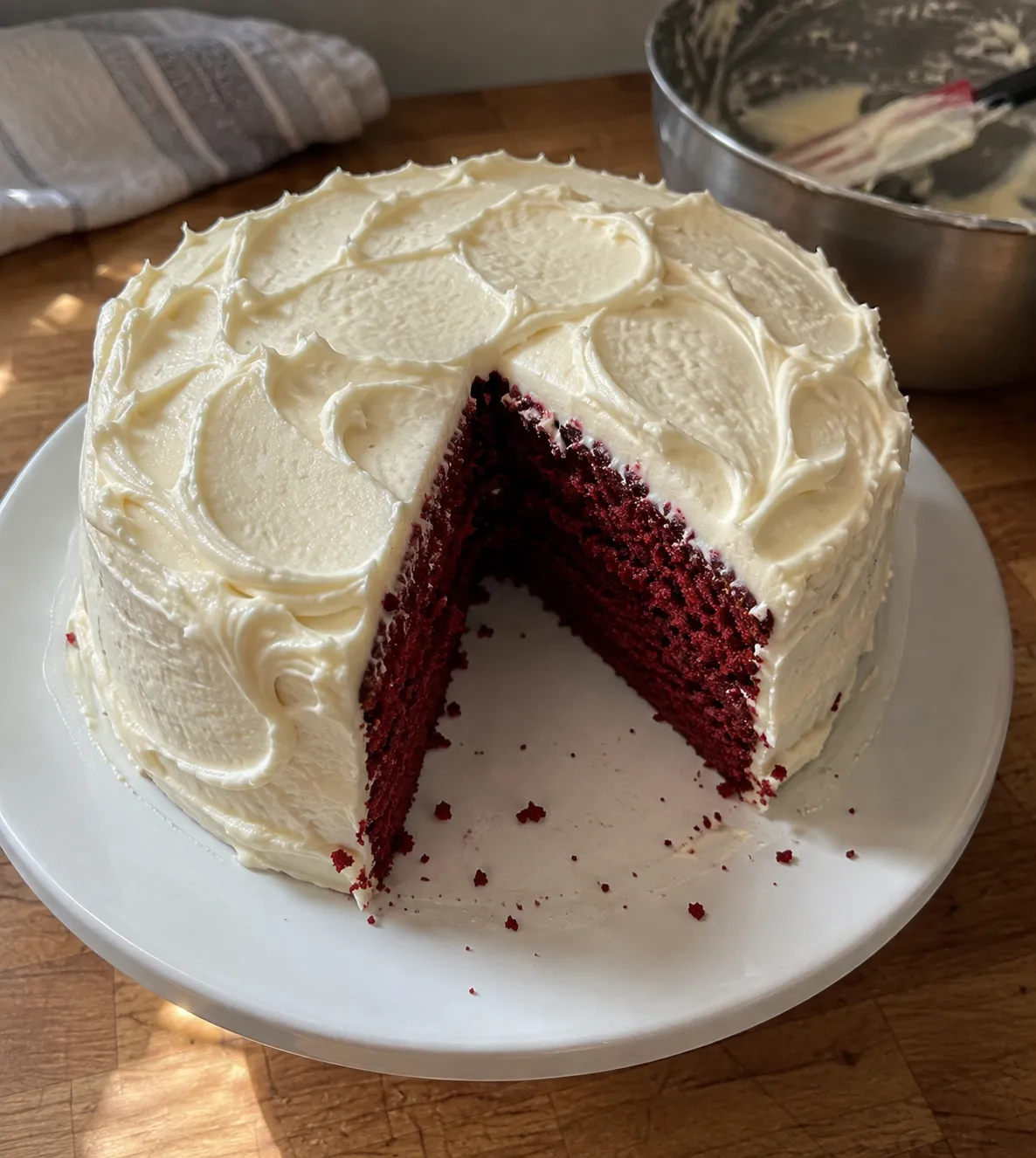 A frosted air fryer red velvet cake with one wedge cut out, showing the deep red crumb against cream cheese frosting