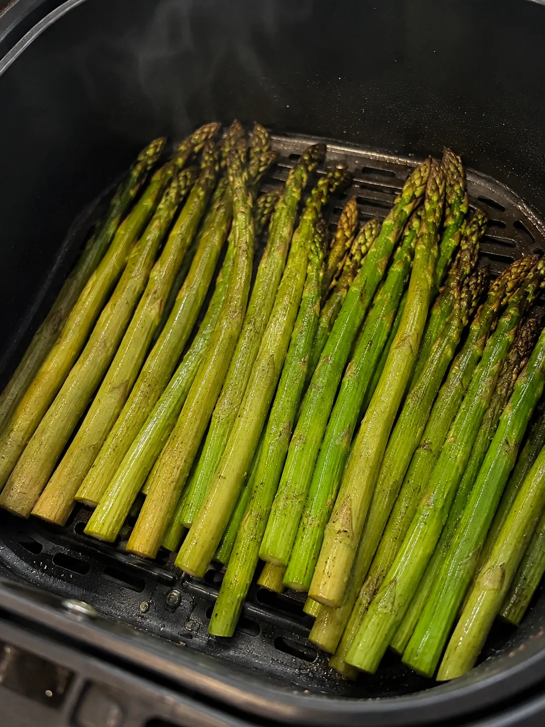 Cooked asparagus steaming in an air fryer basket with browned tips
