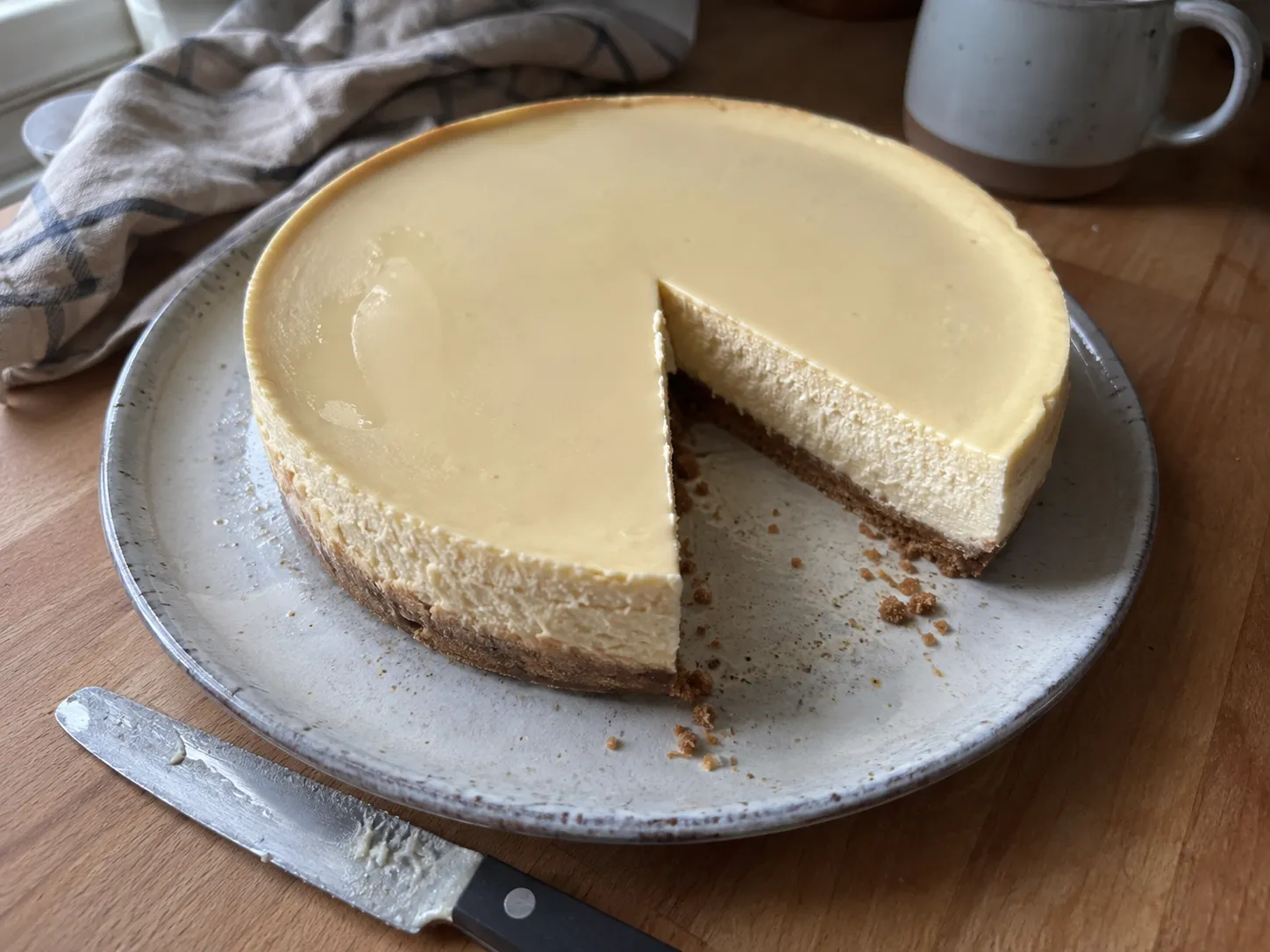 A whole air fryer cheesecake on a plate with one wedge cut out and a smooth uncracked top