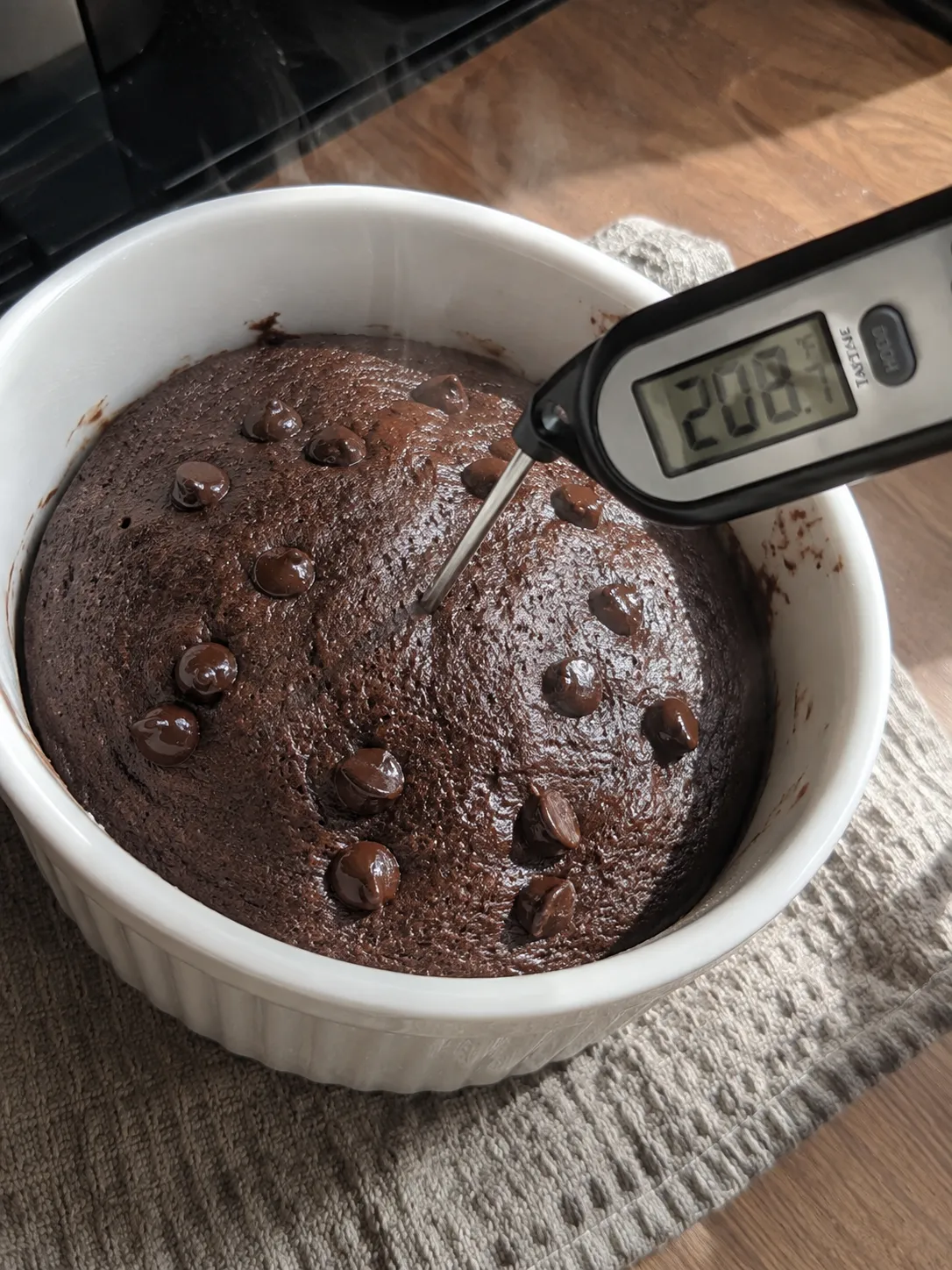 An instant read thermometer pushed into the center of a baked chocolate mug cake, reading 208.7 degrees Fahrenheit