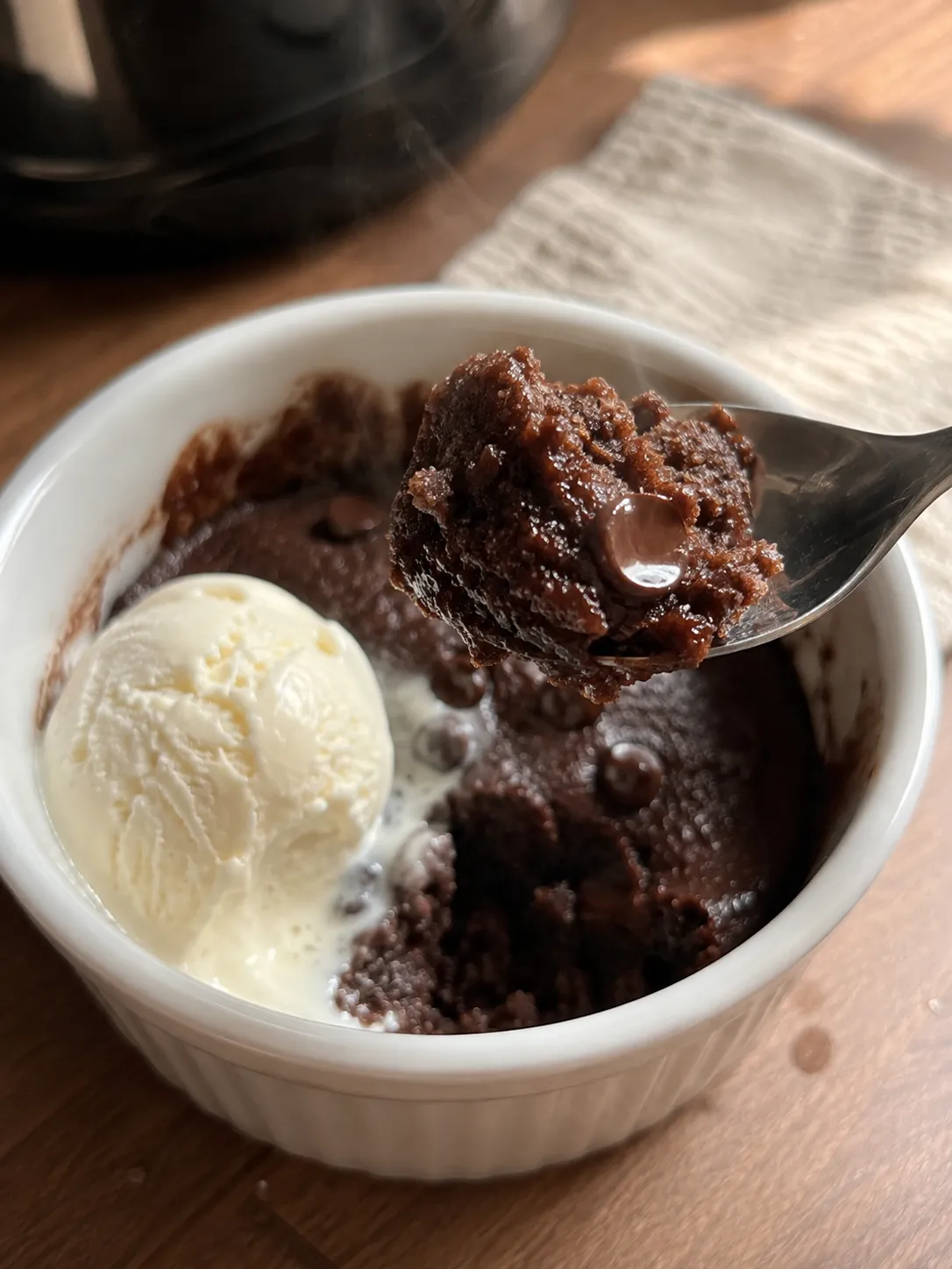 A spoonful of steaming chocolate mug cake lifted from a ramekin with a scoop of vanilla ice cream melting beside it