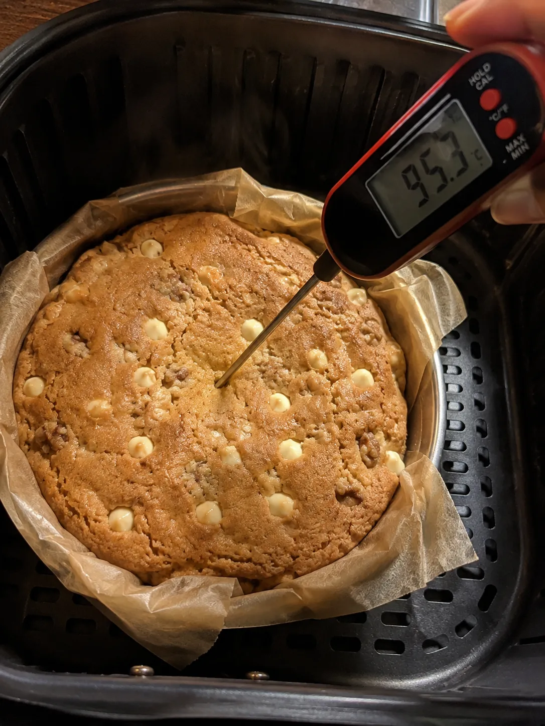 An instant-read thermometer pushed into the center of a golden blondie in the air fryer basket