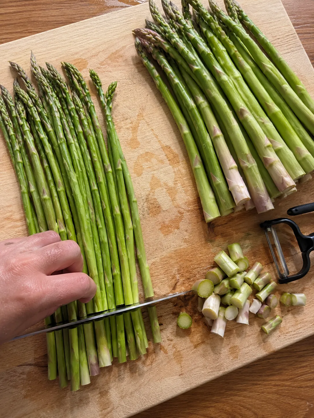 Thin and thick asparagus bunches side by side on a board with the woody ends being cut off