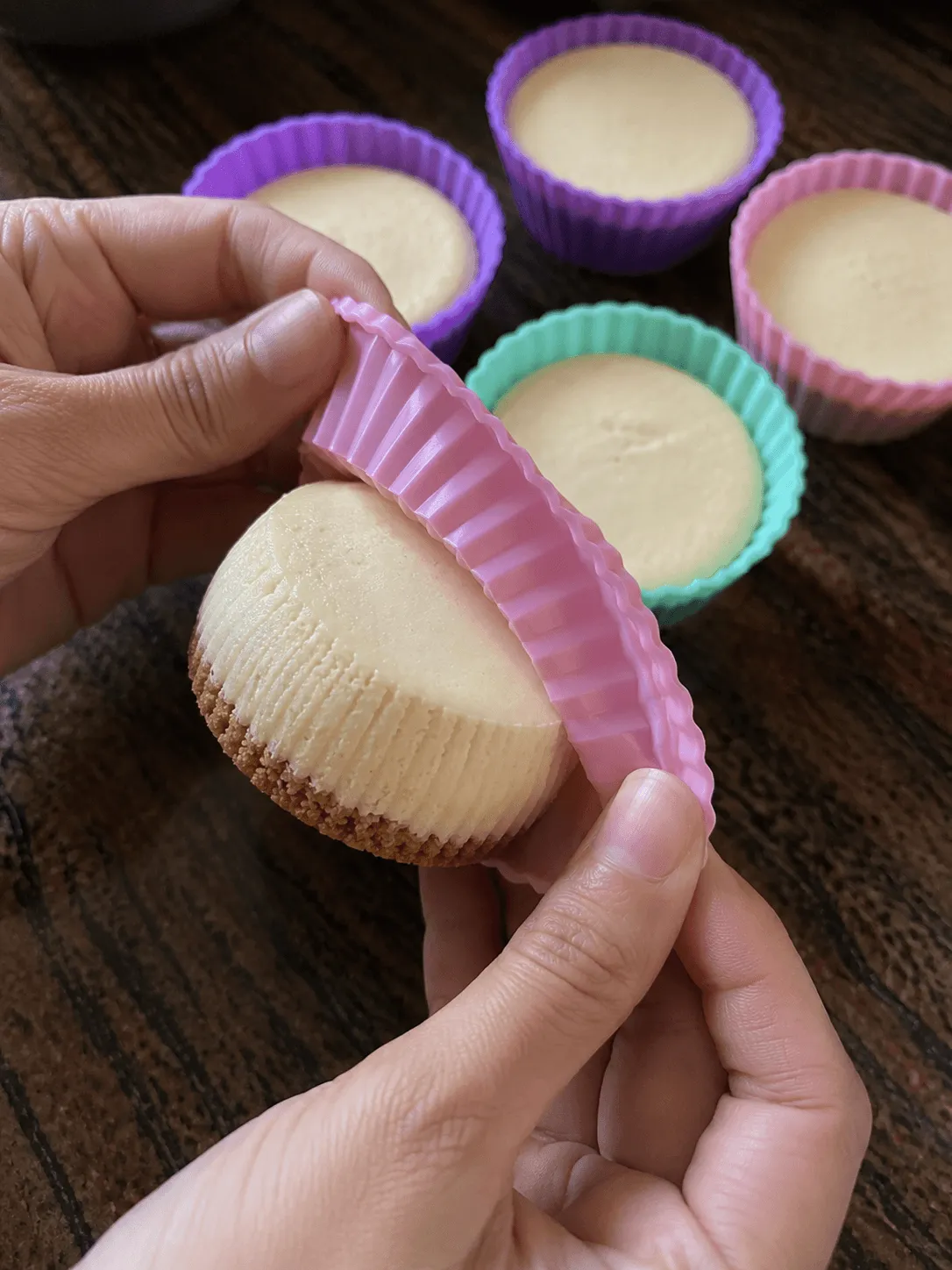 A pink silicone cup being peeled away from a chilled mini cheesecake
