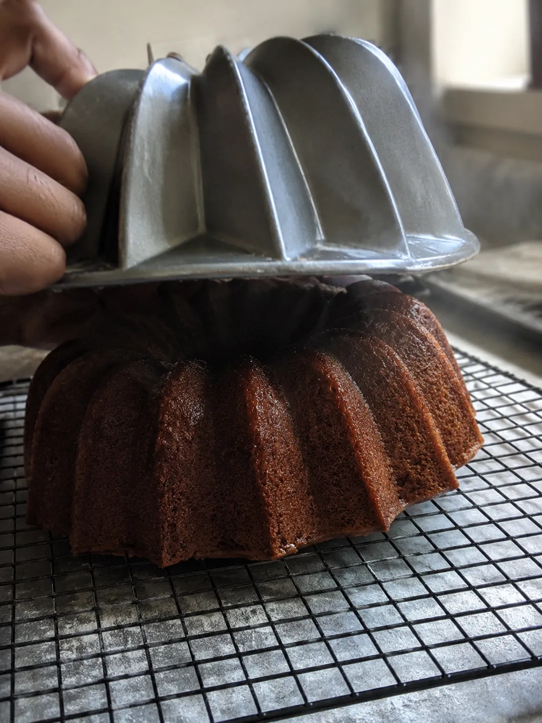 A bundt pan being lifted away from a turned out cake on a wire rack, every fluted ridge intact