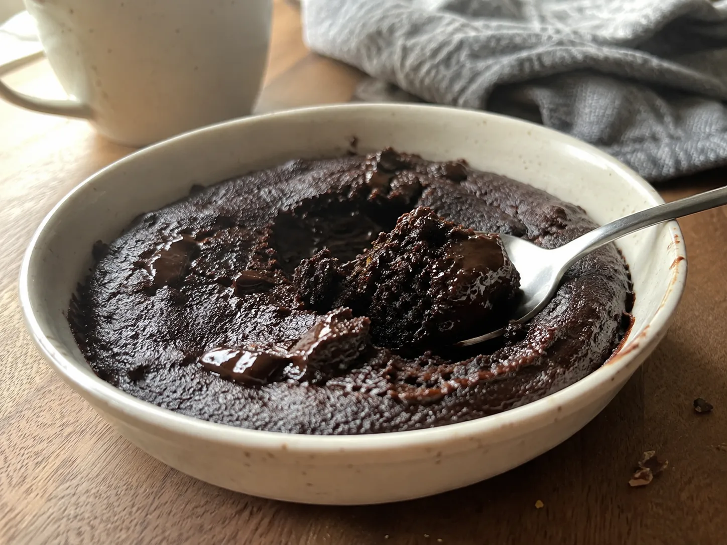 A fudgy air fryer chocolate mug cake baked in a wide shallow dish with a spoon lifting a piece