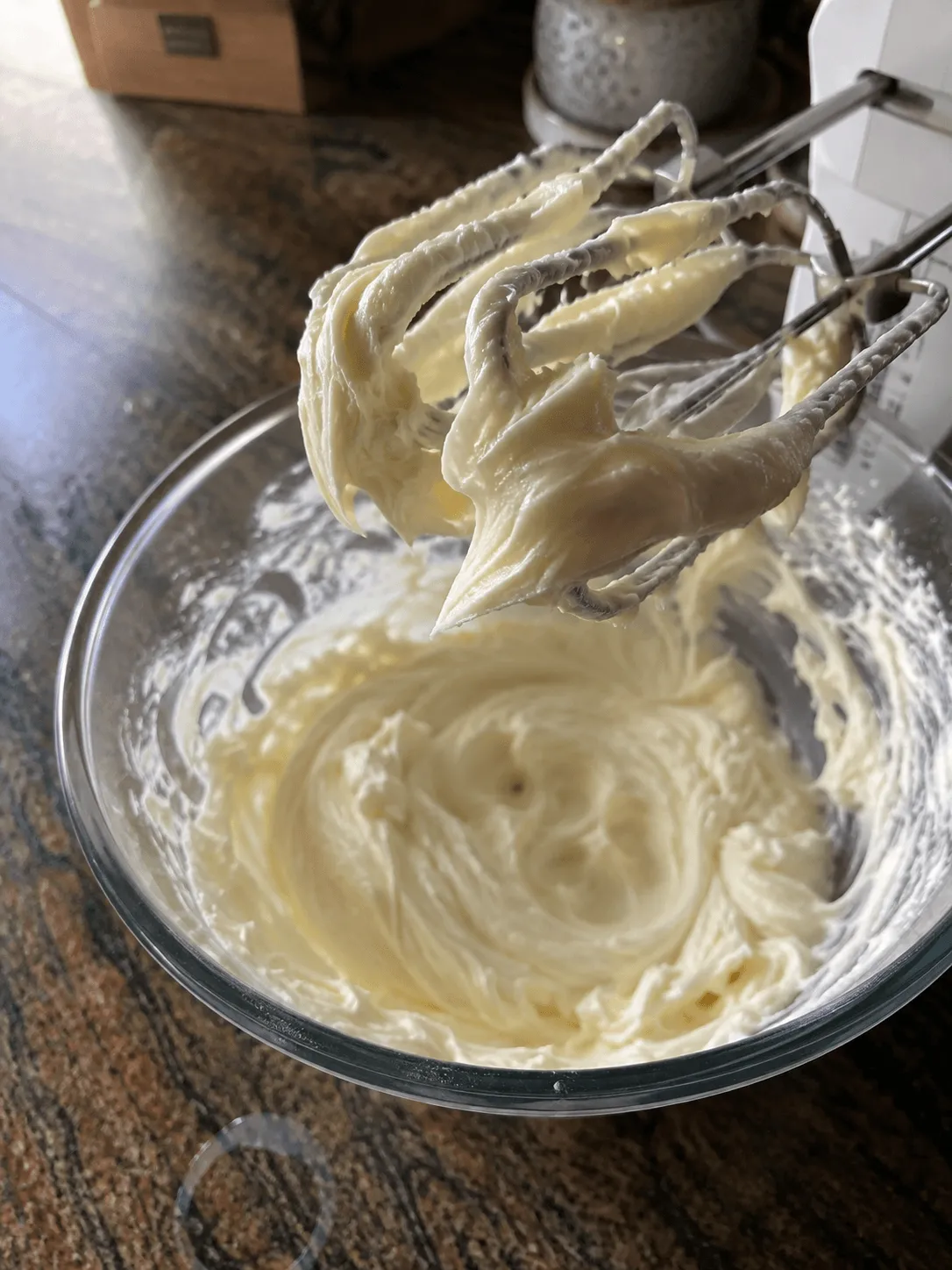 Smooth cheesecake batter clinging to the beaters of a hand mixer above a glass bowl