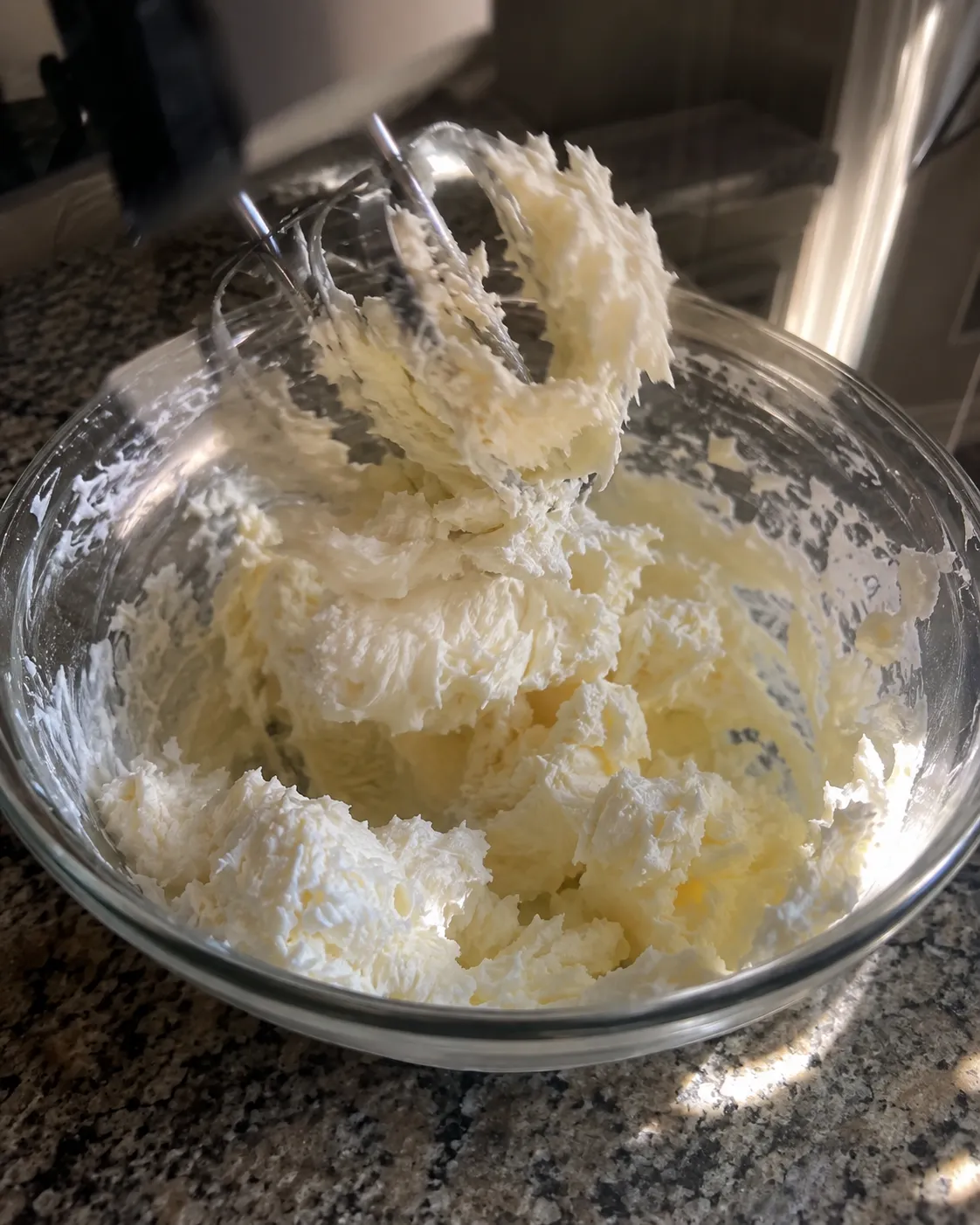 Butter and sugar creamed pale and fluffy in a glass bowl, holding a torn peak on the lifted hand mixer beaters