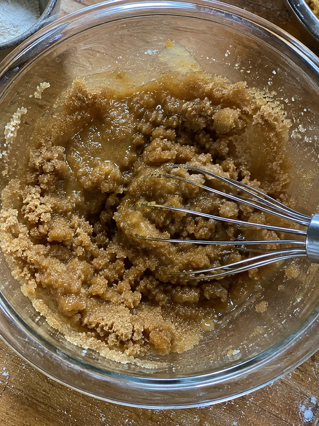 Melted butter and brown sugar whisked together into a grainy, glossy paste in a glass bowl