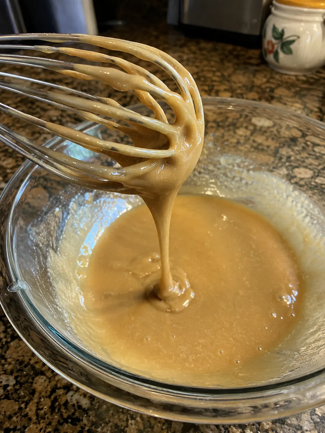 A whisk lifting a smooth ribbon of brown sugar batter out of a glass mixing bowl
