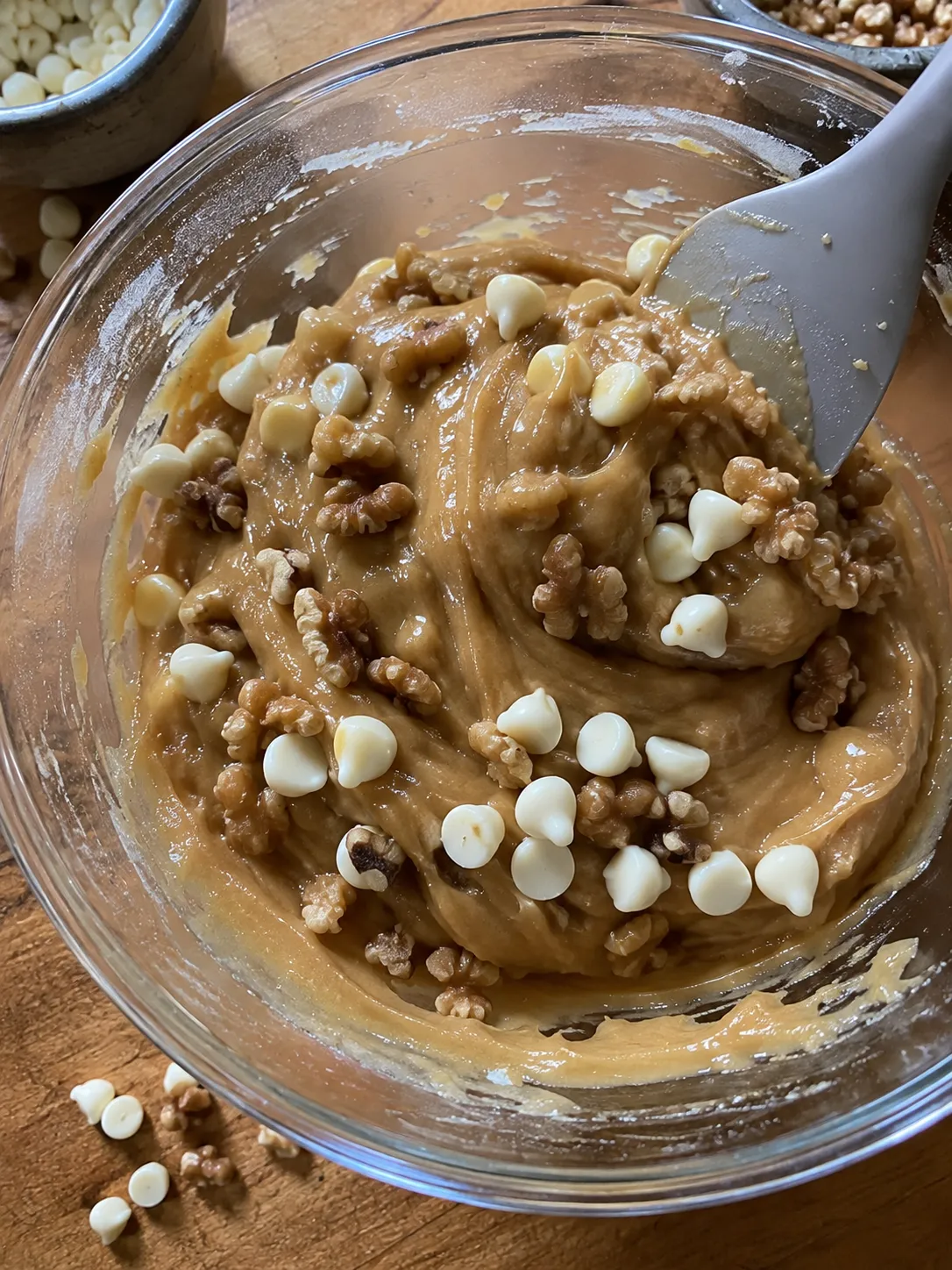 White chocolate chips and walnuts being folded into thick blondie batter with a spatula
