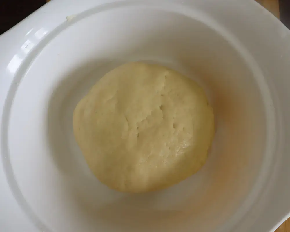 A smooth ball of vegan donut dough resting in a white bowl