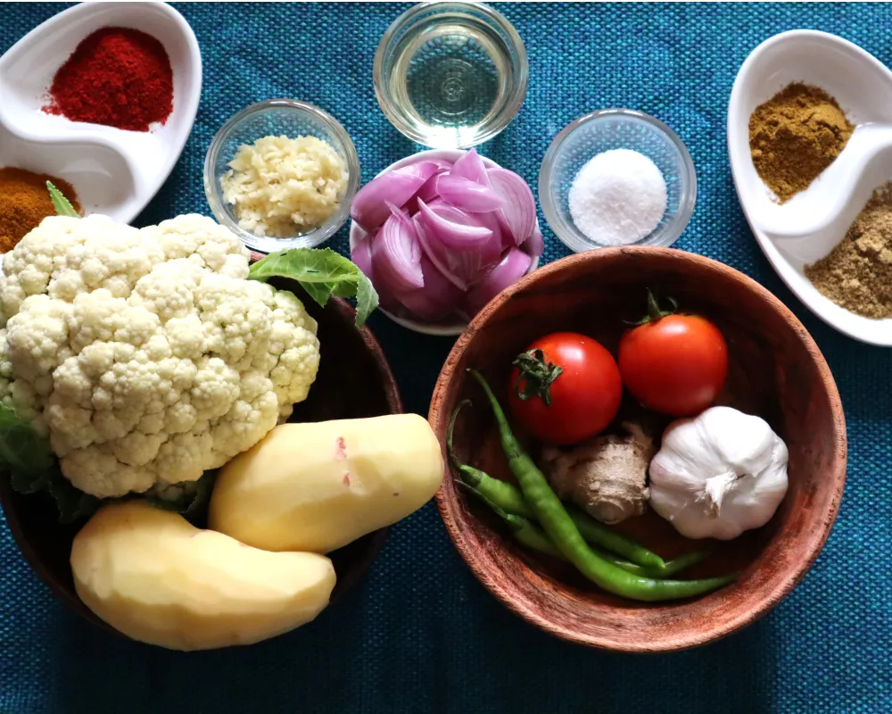 Cauliflower, peeled potatoes, sliced red onion, tomatoes, green chilies, ginger, garlic and bowls of ground spices