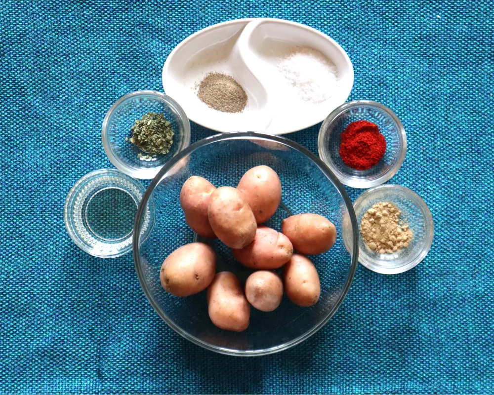 Overhead flat lay of baby potatoes in a glass bowl surrounded by small dishes of salt, black pepper, smoked paprika, garlic powder and dried herbs